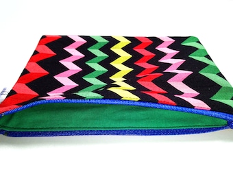 May include: A colorful zippered pouch with a chevron pattern in shades of red, pink, green, yellow, and black. The pouch is lined with green fabric and has a blue zipper.