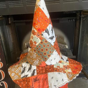 May include: A tall, pointed witch hat constructed from a patchwork of fabric squares featuring various autumn and Halloween-themed prints, including orange pumpkins, black crows, white spiders, sunflowers, and small white floral patterns.