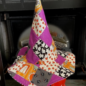 May include: A patchwork witch hat featuring a conical crown and a wide brim, constructed from fabric squares with Halloween-themed prints including orange pumpkins, white ghosts, black cats, and solid purple panels with gold glitter accents.