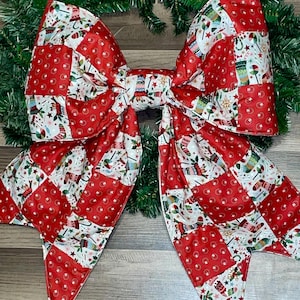 May include: A large Christmas bow with a patchwork design. The bow has red squares with white polka dots and squares with Christmas patterns. The bow is set against a green wreath.