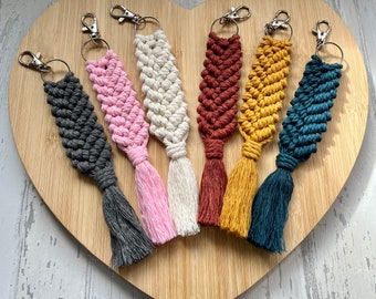 May include: Six colourful macrame keychains with tassels. The keychains are made with a variety of colours, including pink, white, red, yellow, and blue. Each keychain has a silver metal ring.