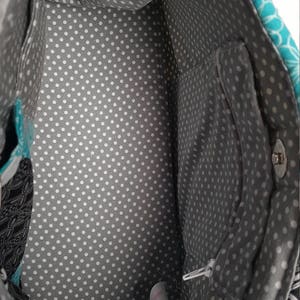 May include: Inside view of a fabric tote bag. The interior lining is grey with white polka dots. The bag has a zipped pocket and a magnetic snap closure. The exterior fabric features patterns in teal, black, and white.