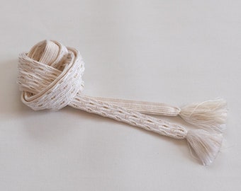 May include: A white, woven cord with a decorative knot and two tassels. The cord is made of a delicate, open weave.
