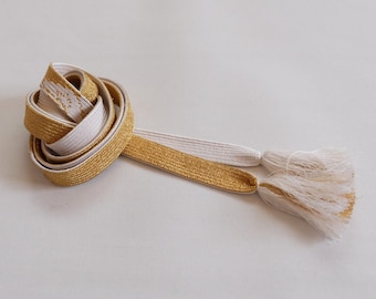 May include: A gold and white cord with tassels. The cord is made of a soft, silky material and has a subtle sheen.
