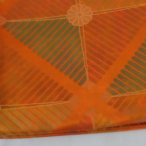 May include: Orange fabric with a geometric pattern of diagonal stripes and stylized flowers. The fabric has a subtle sheen and a soft texture.