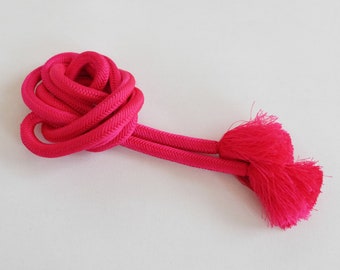 May include: A bright pink cord with two tassels at the end. The cord is tied in a knot and the tassels are hanging down.