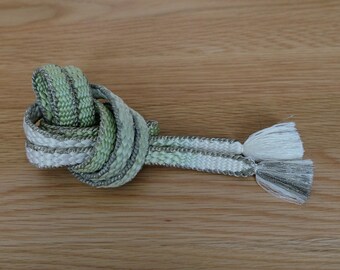 May include: A green and silver braided cord with white tassels. The cord is tied in a knot and the tassels are hanging down.