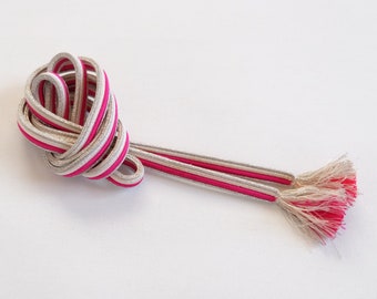 May include: A pair of white and pink cords with tassels. The cords are tied together in a knot.