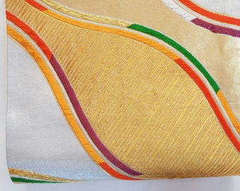 May include: A white fabric with gold, orange, red, and green embroidered lines forming a curved pattern.