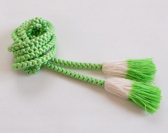 May include: A green braided cord with white and green tassels. The cord is tied in a knot and the tassels are hanging down.