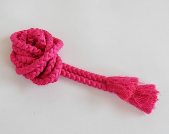 May include: A bright pink braided cord with two tassels at the end. The cord is coiled into a circle and the tassels are hanging down.