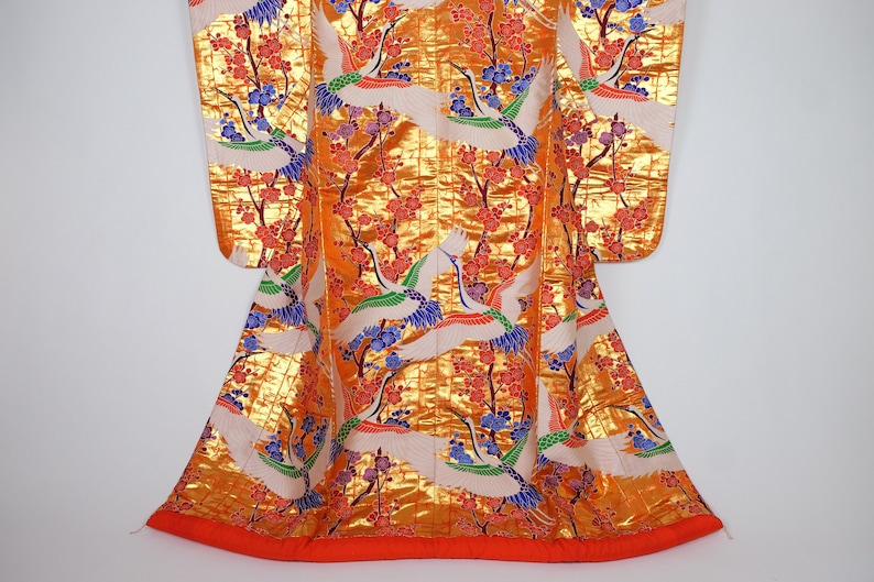 May include: A traditional Japanese kimono with a gold background and a pattern of white cranes flying among red and blue flowers.