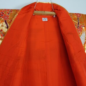 May include: A red kimono with a gold and white floral pattern. The kimono is open to reveal the red lining. The kimono is decorated with cranes and flowers.