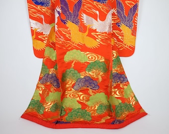 May include: A bright orange kimono with detailed illustrations of cranes and stylized trees. The design features gold accents and a repeating pattern. The kimono's sleeves are visible, showcasing the intricate artwork and rich colour palette.