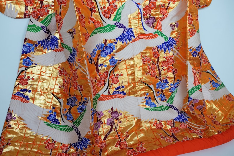 May include: A traditional Japanese kimono with a gold background and a pattern of white cranes flying among red, orange, blue, and purple flowers.