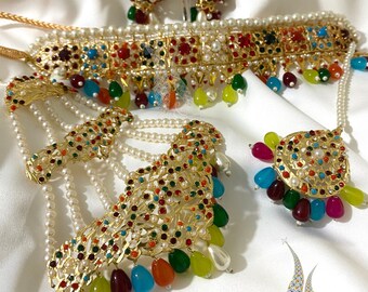 Op de afbeelding: Een gouden kettingset met gekleurde stenen en parels. De set bevat een chokerketting, een lange ketting met een hanger en een paar oorbellen.