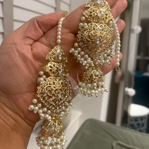 May include: Gold earrings with intricate designs and white pearl accents. The earrings feature a dangling design with multiple layers of pearls.
