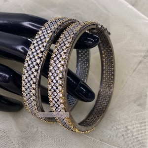 May include: Two silver and gold bangles with a row of clear rhinestones around the circumference.