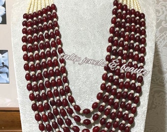 May include: A seven-strand necklace with alternating red and white beads. The necklace is made of red oval-shaped beads and white round beads. The necklace has a gold clasp with red stones.