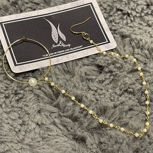 May include: A gold nose ring with a pearl charm and a delicate chain with pearl accents. The nose ring is displayed on a black card with the text "Jewels & Beauty - A Blend of Trend and Tradition".