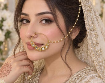 May include: A gold nose ring featuring a circular hoop adorned with multiple white, triangular-shaped stones along the bottom edge. A delicate gold chain embellished with small white beads connects the nose ring to the hair area.