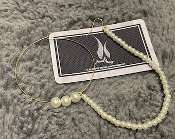 May include: Gold hoop earrings with a pearl drop. The hoop is large and the drop features three pearls. The earrings are on a white background with a card that says "Jewels & Beauty - A blend of trend and tradition".