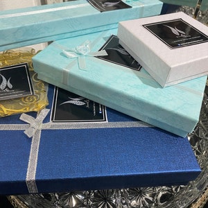 May include: Three blue, white, and light blue gift boxes with a black and white logo that says "Jewelry Beauty - A Blend of Tradition & Modernity" and a website address. The boxes are stacked on top of each other and are sitting on a clear glass plate.