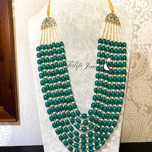 May include: A multi-strand necklace featuring teal-colored oval beads and small white beads. The necklace has gold-colored accents and is displayed on a mannequin. The brand name "Tulip Jewel" is visible on the bottom.