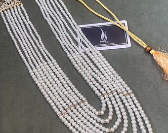 May include: A multi-strand pearl necklace with gold accents and a tassel. The necklace is made of white pearls and has a gold clasp.