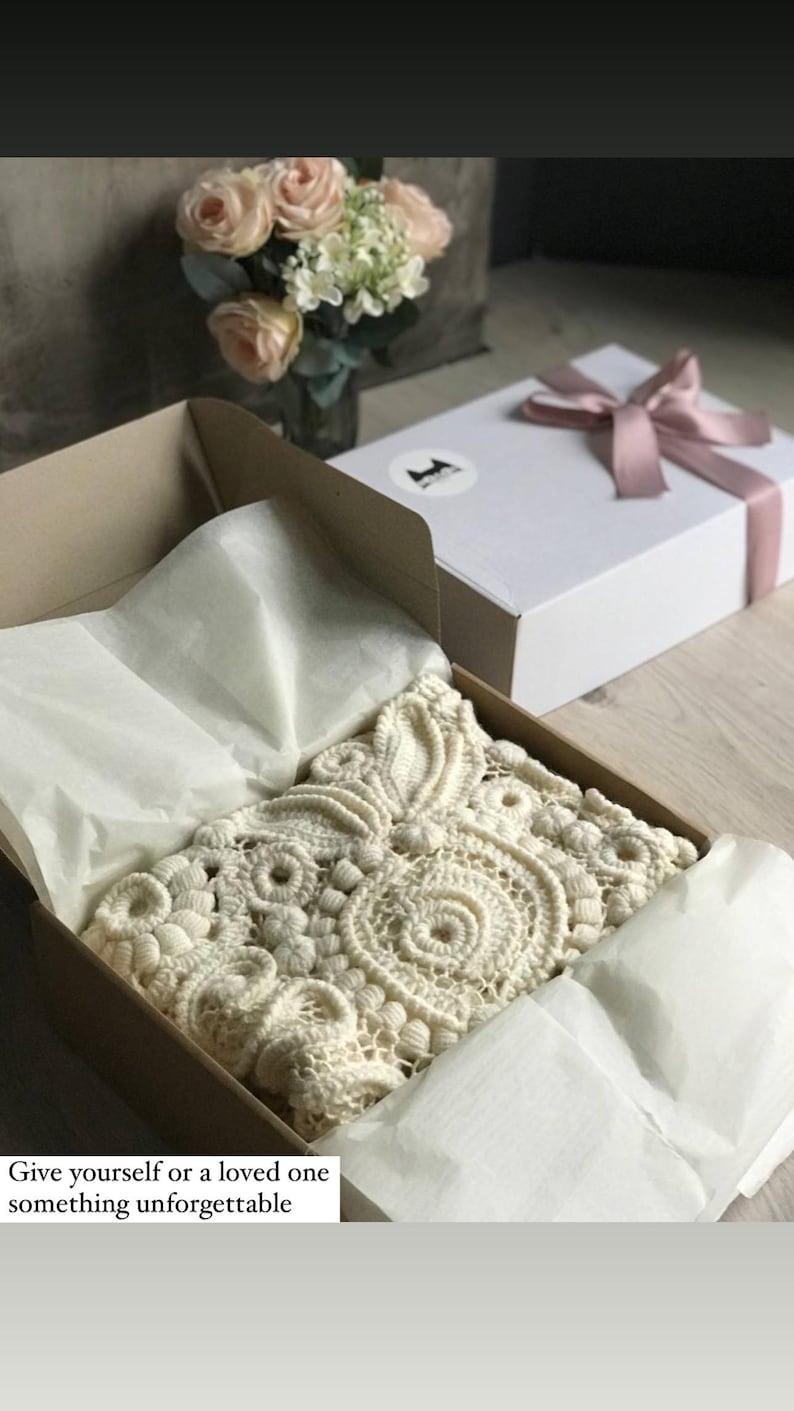 May include: A cream-colored, intricately crocheted item rests in an open cardboard box lined with tissue paper. A white gift box with a pink ribbon sits nearby. The text in the image reads: "Give yourself or a loved one something unforgettable."