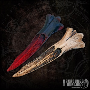 May include: Two carved bone-shaped objects. One is painted with a gradient of red to dark blue, the other is a natural bone color with dark brown accents. The objects have a textured appearance and are displayed on a dark background.