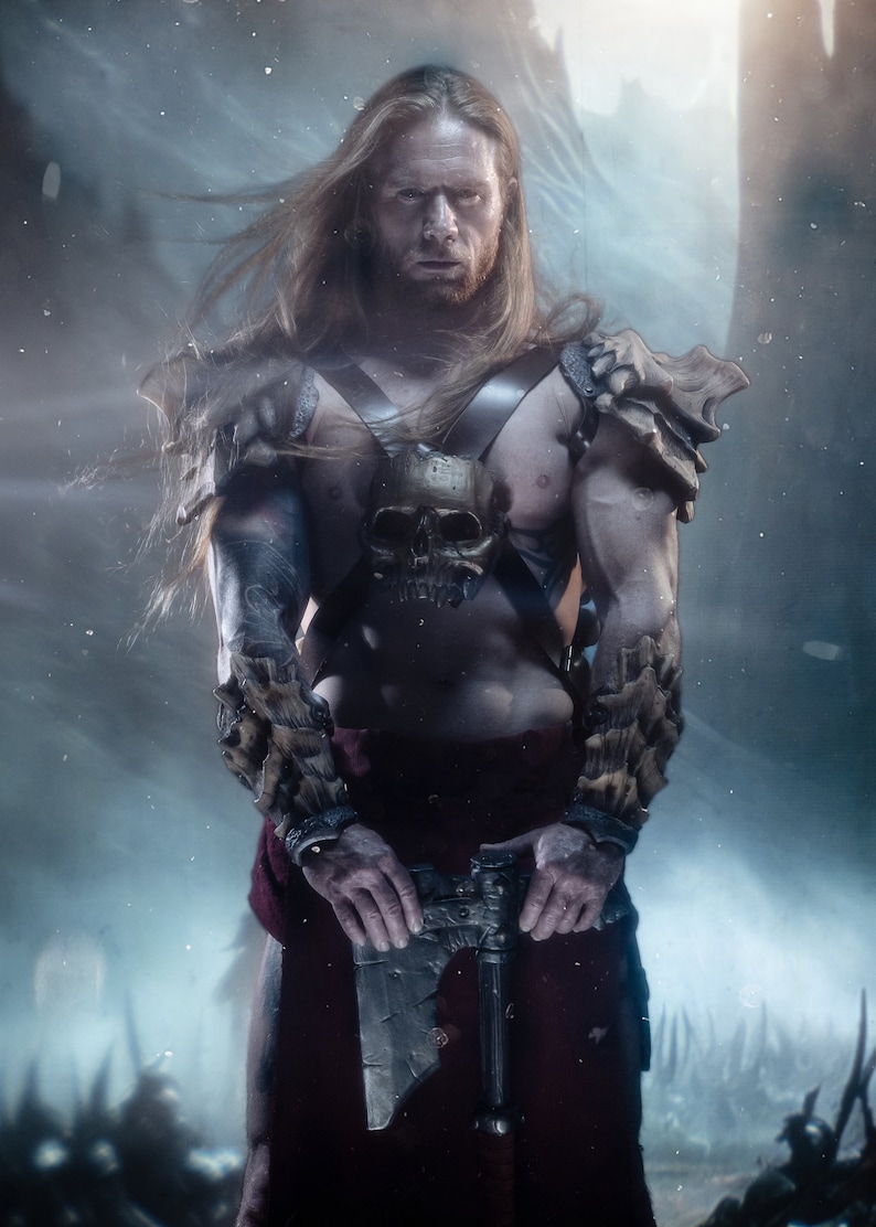 May include: A long-haired warrior with a beard wearing dark leather chest straps featuring a central skull ornament and textured bone-like shoulder and forearm armor. The figure holds a metallic battle axe and wears a dark red cloth garment.