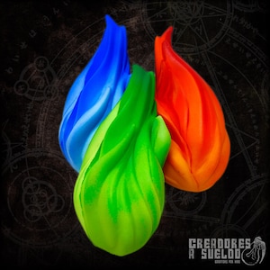 Può includere: Tre oggetti a forma di fiamma in blu vibrante, verde brillante e arancione intenso. Ogni pezzo presenta una consistenza liscia, scolpita e fluida con una finitura opaca. Gli oggetti sono disposti in un gruppo su uno sfondo scuro e decorato.