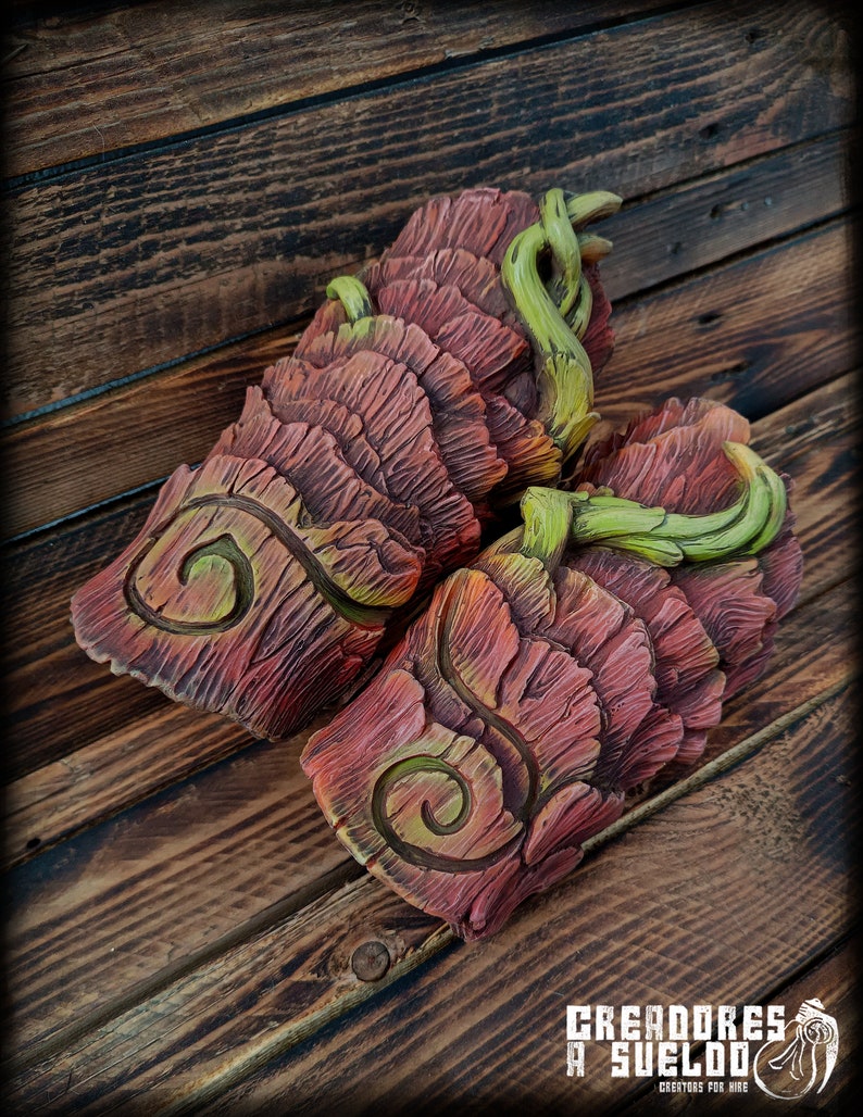 May include: A pair of forearm guards featuring a layered, bark-like texture in shades of reddish-brown. Each piece displays a prominent carved spiral design and is accented with sculpted, light green vine-like elements wrapping around the top edges.