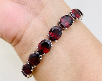 May include: A silver bracelet with a row of oval-shaped red gemstones.