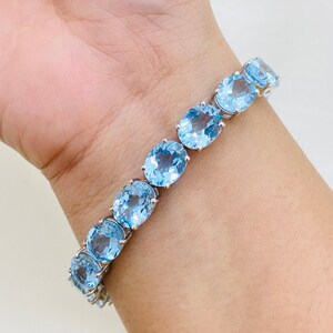 May include: A silver bracelet with oval-shaped blue topaz gemstones. The bracelet is on a person's wrist.