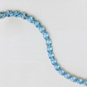 May include: A delicate bracelet made of oval-shaped light blue gemstones set in silver. The bracelet is made of a series of linked gemstones.
