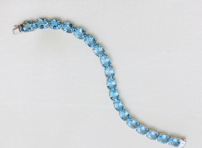 May include: A delicate bracelet made of oval-shaped light blue gemstones set in silver. The bracelet is made of a series of linked gemstones.