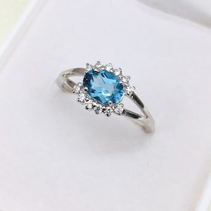 Peut inclure: Une bague en argent avec une pierre ovale bleue entourée de petites pierres claires.