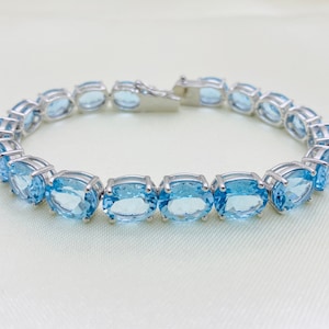 May include: A silver bracelet with a row of oval-shaped blue topaz gemstones.