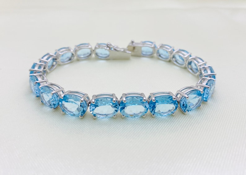 May include: A silver bracelet with a row of oval-shaped blue topaz gemstones.