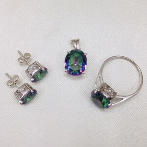 May include: A silver ring, pendant, and earrings set with iridescent green and blue gemstones. The ring has a simple band and a large oval-shaped gemstone. The pendant is a simple design with a large oval-shaped gemstone. The earrings are small and have a simple design with a small oval-shaped gemstone.