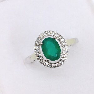 Peut inclure: Une bague en argent avec une grande pierre précieuse ovale verte entourée d'un halo de petites pierres précieuses blanches.