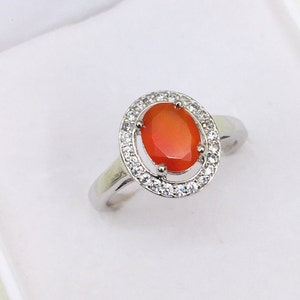 Peut inclure: Une bague en argent avec une grande pierre ovale orange entourée d'un halo de petites pierres claires.