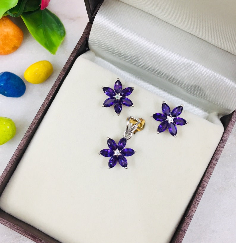 May include: A set of amethyst flower earrings and a matching pendant necklace. The jewelry is displayed in a white velvet box.