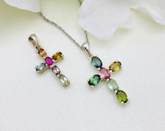 Puede incluir: Dos colgantes de cruz de plata con piedras preciosas de colores. El colgante más grande tiene un diseño de piedras preciosas verdes, azules, rosas y amarillas. El colgante más pequeño tiene un diseño de piedras preciosas rosas, verdes y amarillas.