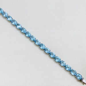 May include: A silver bracelet with a row of oval-shaped light blue gemstones.