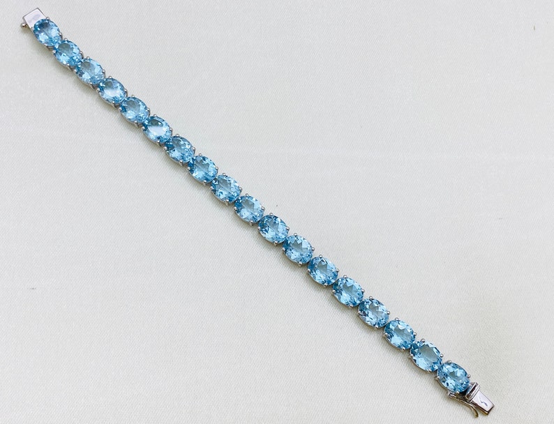 May include: A silver bracelet with a row of oval-shaped light blue gemstones.