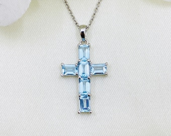 Puede incluir: Un collar de plata con un colgante en forma de cruz. La cruz está hecha de piedras preciosas de color azul claro.