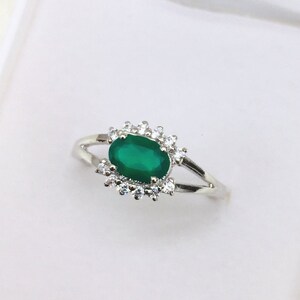 Peut inclure: Une bague en argent avec une pierre ovale verte entourée de petites pierres claires.